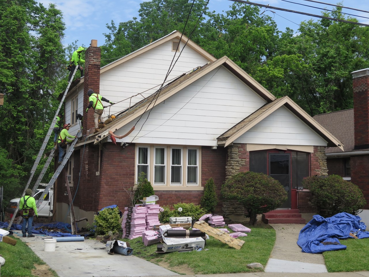 A crew from Deer Park Roofing works to install a new roof on Naima Jackson's home on May 24, 2021. Ladders are extended so crews can reach two levels of roofing, and materials are stacked in Jackson's front yard.
